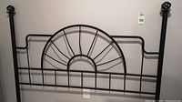 Full view of black metal headboard with sunburst central design and spiral finials on each post.
