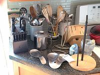 Full view of knife block, cooking utensils holder with wooden and metal utensils, metal paper towel holder, mortar and pestle, spoon rests, and banana hook on countertop