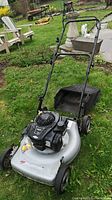 Full view of the Murray lawn mower on grass, showing mower deck, handle, rear bag, and wheels.