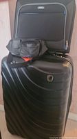 Leo by Heys black hard sided suitcase with four wheels, Solo black leather-like fanny pack, and Solo black carry-on bag stacked together.