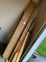 Photo showing lumber pieces including long 2 x 4 and 1 x 10 boards with orange two-foot spirit level and black metal builder's square resting against the wall near a door