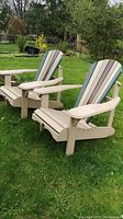 Photo showing two painted wood Muskoka chairs positioned outdoors on grass with multi-colored vertical slats on backrests and beige armrests and seats.