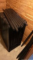 Stack of 12 black plastic shelving pieces with grid design and poles stacked horizontally on top.