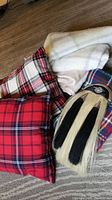 Four blankets with different patterns including plaid and plain beige, two plaid cushions with Life at Home tags, and a traditional kilt sporran with horsehair and metal thistle crest.