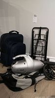 Steam Shark Euro Pro X steam cleaner in silver next to a folding cart and a backpack bag displayed against a white wall.