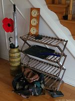 Photo of shoe rack and umbrella stand with bags, umbrellas and weather station under the stairs.