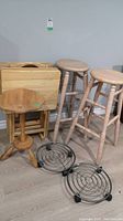 Two wood stools, wooden pedestal table with plant coasters beneath, set of folding tray tables behind