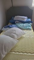 View of upholstered headboard at the back, mattress with foam topper and folded bedding on top