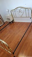 Bed frame including brass tone metal headboard and footboard with heart-shaped design, pictured in room with hardwood floor.