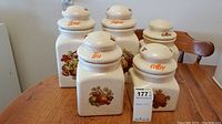 Set of five ceramic labeled canisters on a wooden table, showing overall condition and design
