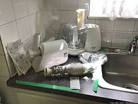 Photo showing the Braun hand mixer, Moulinex grinder, and Black and Decker processor arranged on a kitchen counter, some accessories and cords visible.