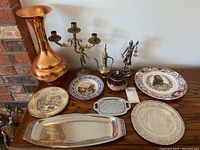 Copper vase, brass candelabra, decorative plates, small brass kettle, ceramic jar, metal tray and Lady Justice figurine arranged on table