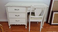 Front view of white wooden desk with three drawers and matching chair showing decorative handles and curved legs on desk.
