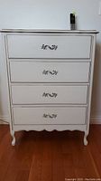 Front view of the white wooden dresser showing four drawers with decorative metal handles and curved bottom edge.