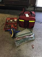 Photo of red emergency kit bag, plumbing tool kit with assorted fittings and gauges, plumbing drain snake, and mesh bags.