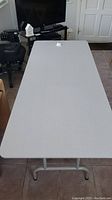 Full top view of a long rectangular folding table with light gray laminate surface placed on tiled floor, showing overall size and condition.