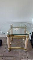 Full view of glass top side table with rounded square edges and brass frame.