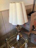 Full view of the vintage glass and brass table lamp with cream pleated shade on a glass table, showing overall size and design.