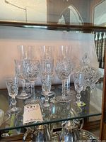 Wide shot of multiple Pinwheel crystal stemmed glasses and a lidded candy dish on glass shelf, some glasses appear chipped