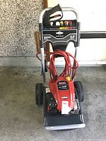 Front view of entire pressure washer showing frame, engine, hose and wheels