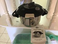 Pressure cooker displayed with instruction booklet visible in front, showing overall condition and included materials.