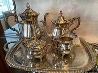 Full view of the silver plate tea set pieces displayed on an ornate silver tray showing teapots, sugar bowl, and creamer.