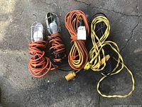 2 handheld trouble lights with protective cages and two extension cords on concrete floor.