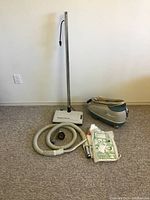 Full lot overview showing compact Electra vacuum body, chrome wand, Sweep n Groom power head, hose, attachments, and vacuum bags spaced on carpet.