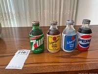 Four vintage unopened glass pop bottles on a wooden surface next to a receipt, including 7UP, Schweppes Tonic Water, Schweppes Club Soda, and Pepsi.