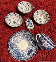 Top down view of all five pieces on red textured surface, showing cups, saucer and bottle details