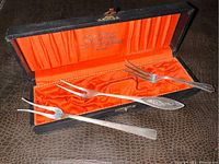 Three sterling silver cocktail forks displayed inside original black hinged presentation box with orange satin lining and gold lettering.
