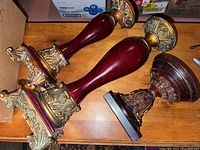 Grouped photo of three red and gold candle holders with ornate details on a wooden surface