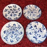 Four antique Chinese porcelain saucers with varied blue hand painted floral patterns shown from above on red textured fabric.
