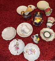 Wide view of all items on red carpet background, showing full assortment including plates, cups, creamers, and sugar bowl