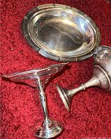 All three pieces on red carpet background showing two silver pedestal bowls and one oval silver plate tray