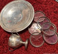 Photo showing large sterling silver serving bowl, sugar bowl with handles, and six round cut glass coasters with silver edging on a red carpet background.