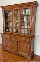 Front view of vintage solid wood two piece cabinet showing three glass doors on upper section and three drawers with three doors below.