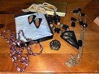 Overview of jewelry lot with necklaces, earrings, and pin arranged on wood surface.