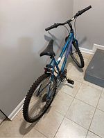 Photo showing side and rear angle of worn blue bicycle with black seat, one flat tire, and gear system.
