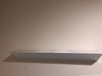 Front view of white floating shelf mounted on a beige wall, showing flat surface and length.