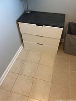 Photo of small 3 drawer dresser in corner on tiled floor, showing white body and custom dark top.