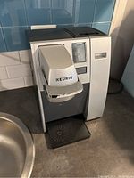 Front view of Keurig coffee maker showing the brewing unit, drip tray, and part of the water reservoir.
