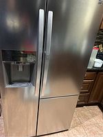 Full view of stainless steel Kenmore refrigerator with side-by-side doors and bottom freezer drawer, featuring water dispenser on left door.