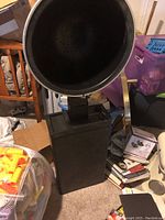 Black large hair drying hood mounted on black rectangular base, placed on carpeted floor near furniture and other household items.