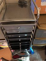 Front view showing multiple black drawers with chrome knobs and part of chrome tubular frame on rolling cart
