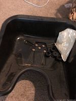 Top-down view of black shampoo bowl showing drainage hole and mounting parts inside.