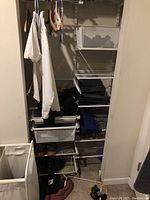 Closet view showing multiple white wire shelves installed with clothes and miscellaneous items on them. Shelving attached or stacked without visible wall brackets. Clothes racks above shelves.