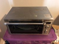 Front view of the Delonghi toaster oven showing stainless steel body, glass door with stainless handle, control knobs on the right.