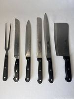 Full view of Rostfrei 6-piece set consisting of five knives with different blade designs and one carving fork, all with black handles and stainless steel blades showing signs of use.