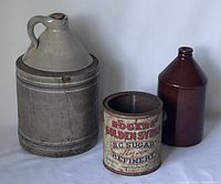 Front view of all three items: two stoneware jugs and one Rogers Golden Syrup tin